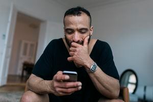 A gay man smirking while reading some messages and responses from people on a dating app with his smartphone.