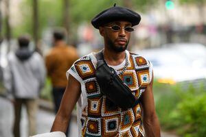 Un invitado lleva una boina de fieltro negra, gafas de sol negras, una riñonera de cuero negro brillante, un collar de cadena de plata, un jersey sin mangas con estampado de cuadros en blanco con marrón y verde oscuro, una mezclilla azul con ovejas blancas chaqueta interior, fuera del show de Hermes, durante la Semana de la Moda de París - Moda masculina Primavera/Verano 2023, el 25 de junio de 2022 en París, Francia.