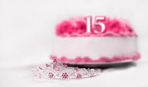 A tiara worn by a girl celebrating her 15th birthday is shot in front of a birthday cake. The focal point is on the tiara.