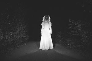 Una mujer, se enmascaró en una bruja aterradora para Halloween, de pie en la calle, en blanco y negro.