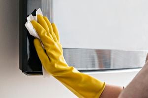 Woman cleaning the TV with damp cloths and wearing yellow gloves during coronavirus, covid 19 quarantine. Maintain hygiene at home, clean dust and bacteria, clean viruses from television.