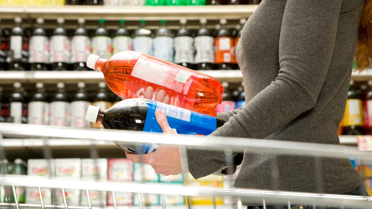 Mujer comparando ingredientes en botella de refresco, botella de gaseosa