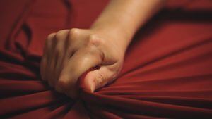 Woman hand passionately squeezes red bed sheet. Love concept.