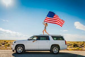 Hispanic woman waving American flag on roof of white SUV