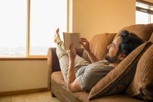 Hispanic man reading book on sofa