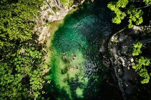 Extreme wide shot aerial view of friends relaxing in cenote at eco resort in jungle