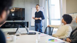 Mature businessman giving presentation to colleague. Group of diverse business people brainstorming in meeting.