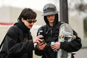 PARIS, FRANCE - JANUARY 22: A guest (L) wears sunglasses, a black scarf, a black long coat, a black and orange print pattern sweater, a guest (R) wears a gray bob hat, silver ring, a black rain coat, outside Loewe, during Paris Fashion Week - Menswear F/W 2022-2023, on January 22, 2022 in Paris, France. (Photo by Edward Berthelot/Getty Images)