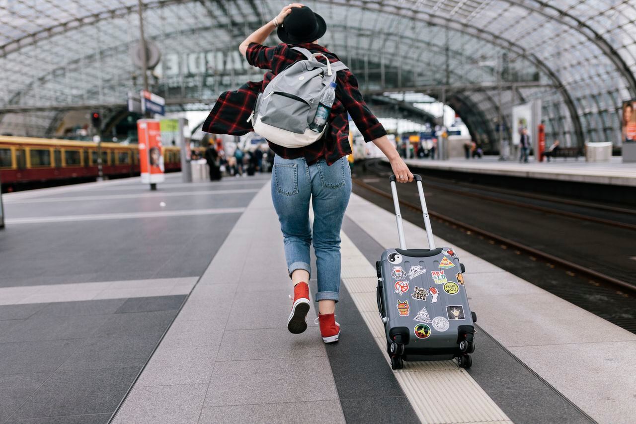Mujer corriendo en medio de una estación de tren con sus maletas