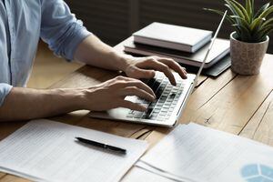 Hombre de negocios de cerca usando una computadora portátil, escribiendo en el teclado, sentado en un escritorio de madera con documentos, escribiendo un correo electrónico, contable escribiendo un informe financiero, estudiante ocupado estudiando en línea, buscando información