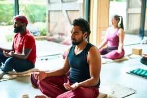 Man wearing black vest in his 40s sitting with eyes closed, cross legged, introspection, meditation, mudra