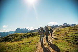 Backview of father with his teenage daughter and teenage son, all carrying a large backpack while hiking on a pathway in the Alps ("Rosengarten") on a sunny and almost cloudless day in summer