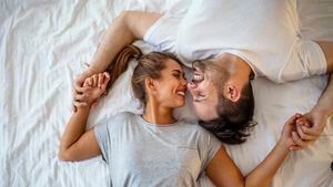 Chico y chica en un acogedor ambiente hogareño. Hombre y mujer felices acostados en la foto de stock del dormitorio. Vista superior de una pareja joven sonriente abrazándose en la cama por la mañana. Hermoso par de amantes abrazo y beso