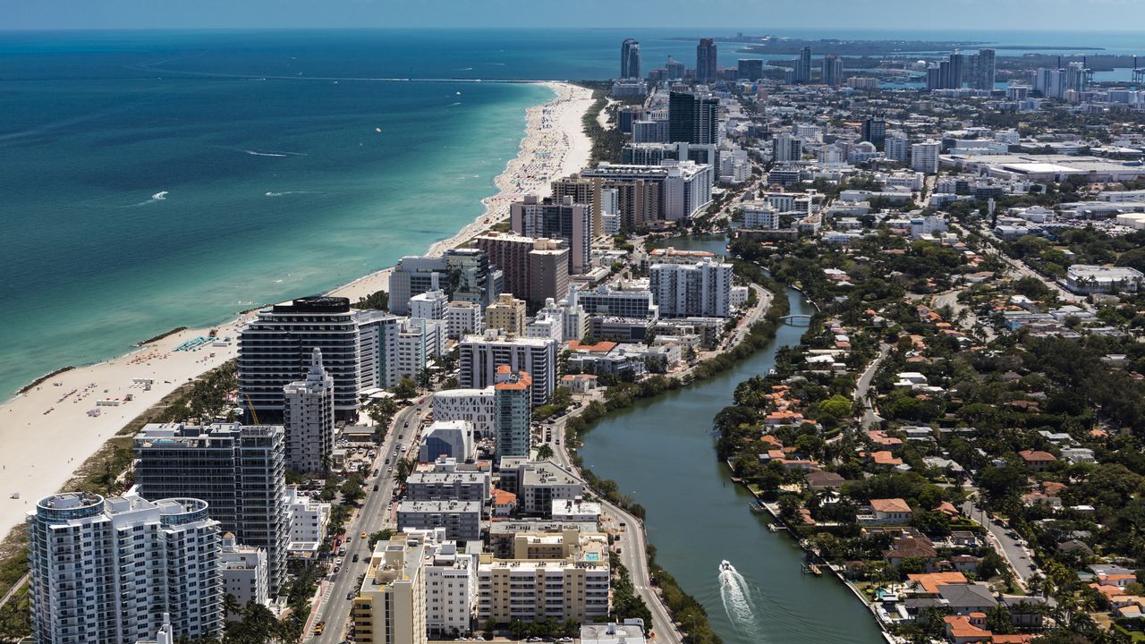 Aerial view of South Beach Miami Florida cityscape with buildings along the beach on a beautiful sunny day, people on beach and ocean, Collins Ave., and boat on Indian Creek