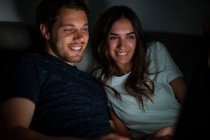Cheerful couple watching online content on laptop during nightime