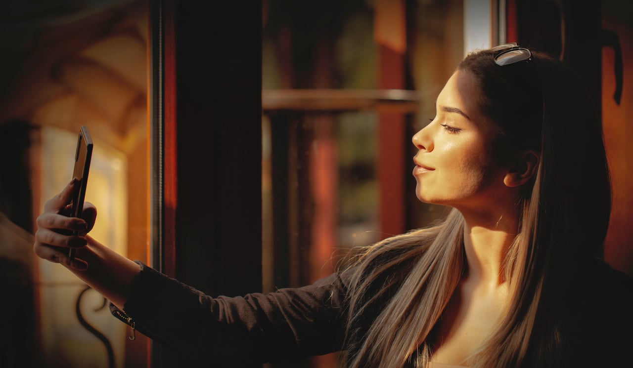 Young woman sitting at cafe and making selfie photo