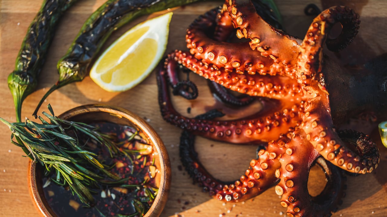 Delicious grilled octopus on metal grill seafood bbq with chili sauce, herbs and rosemary. Octopus with green sweet pepers, chili-lemon sauce - traditional Mediterranean dish or Asian cuisine.