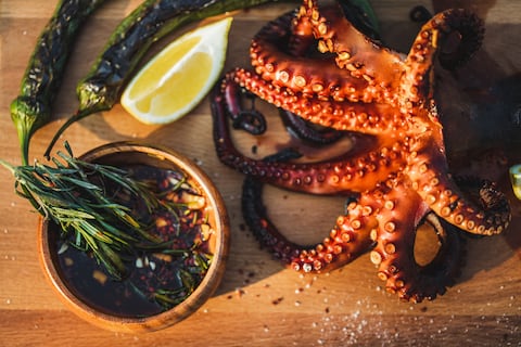 Delicious grilled octopus on metal grill seafood bbq with chili sauce, herbs and rosemary. Octopus with green sweet pepers, chili-lemon sauce - traditional Mediterranean dish or Asian cuisine.