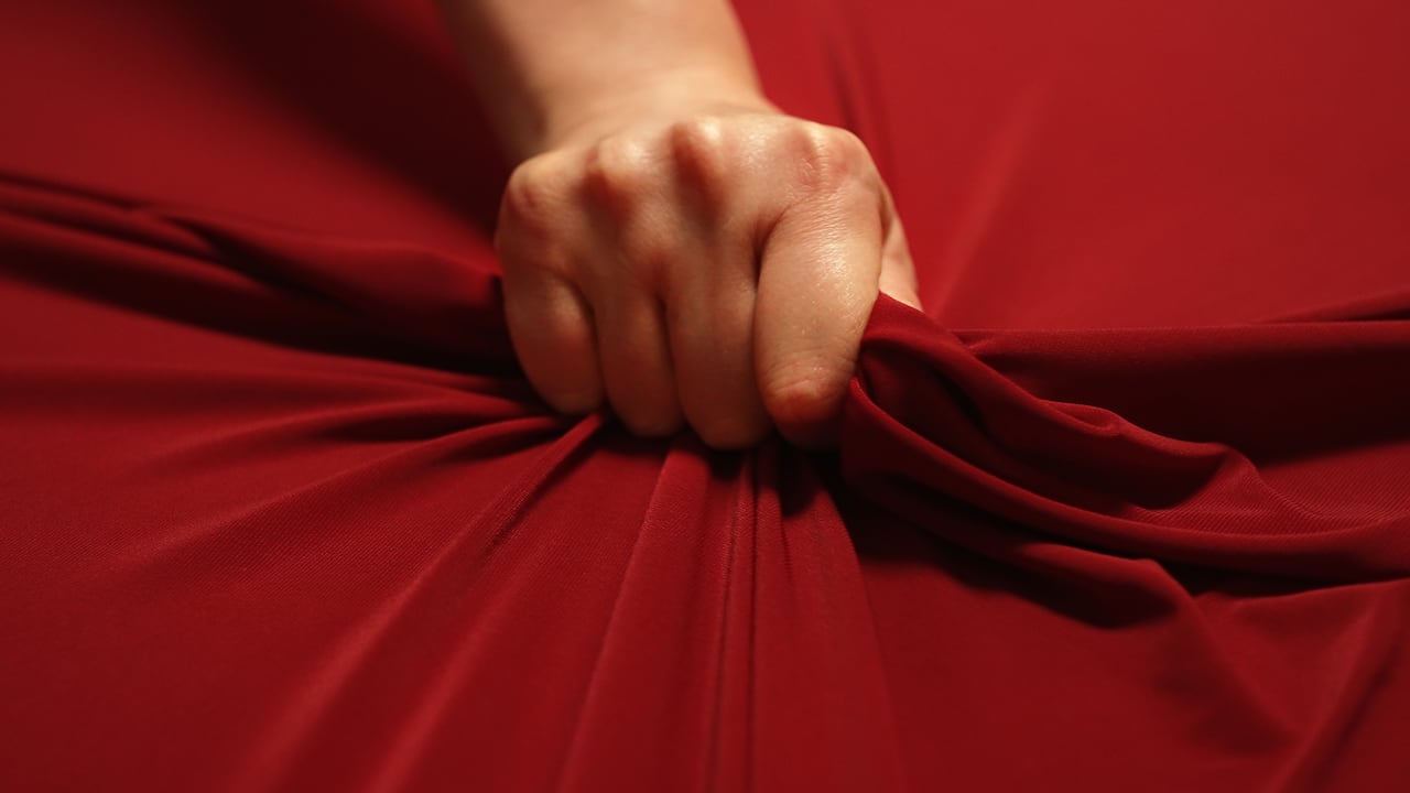 Woman hand passionately squeezes red bed sheet. Love concept.