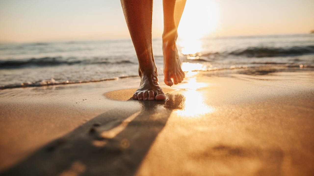 Close-up of female legs getting out of the sea water and walking on sandy beach at beautiful sunset