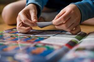 Zurich, Switzerland - April 16, 2016: An 8 year old boy is sitting on the floor of his room and is pasting football trading cards into his sticker collection scrapbook for the UEFA Euro 2016 Euopean football championship.
