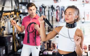 Woman and man purchasers looking black collar and leather lash in the sex shop