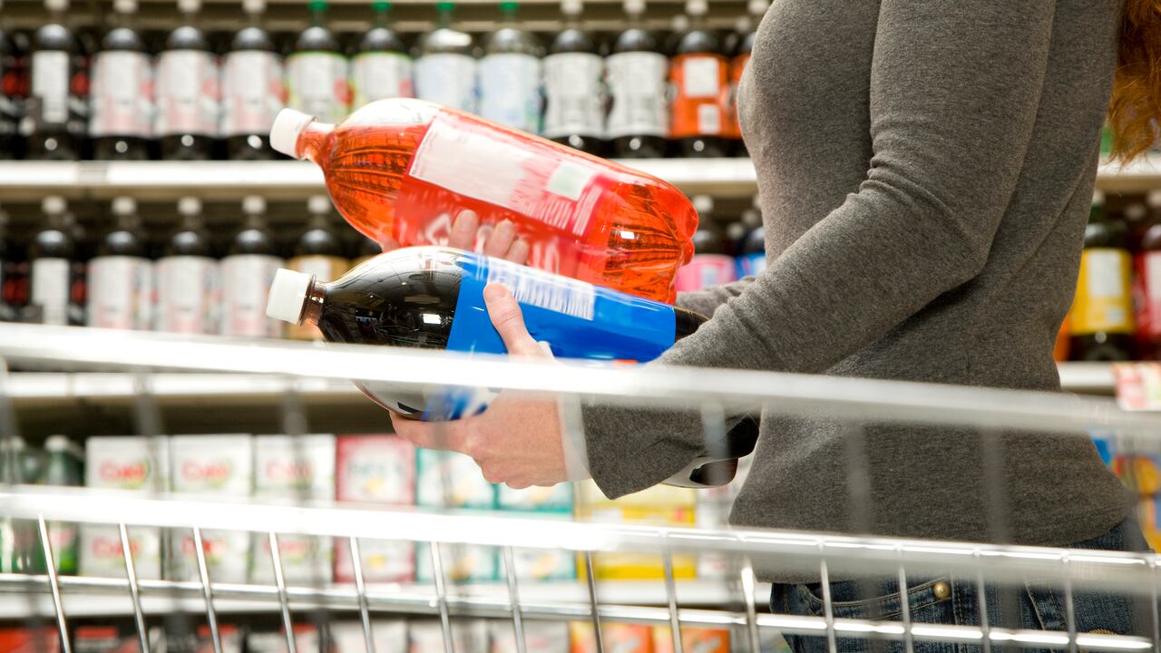 Mujer comparando ingredientes en botella de refresco, botella de gaseosa