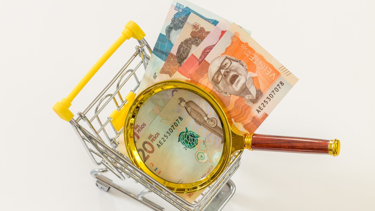 A miniature shopping cart with Colombian money and a magnifying glass. Economic and business concept, rising inflation and the country's economic upset. White background