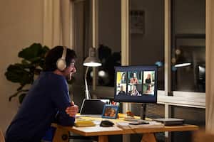 Side view of male freelance worker discussing during video call with colleagues. Smiling businessman is sitting at table in home office. He is working late at night.