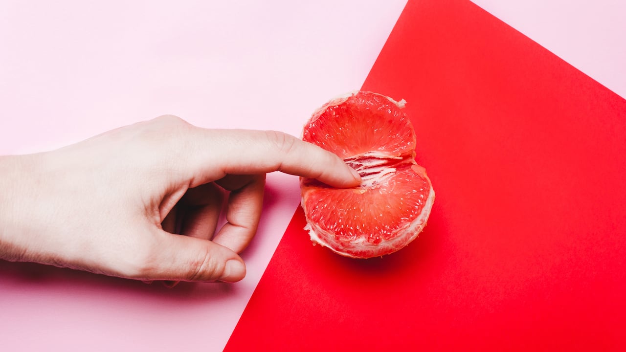 Concept sex, masturbation. Hand, fingers in grapefruit, vagina symbol on a red background