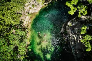 Extreme wide shot aerial view of friends relaxing in cenote at eco resort in jungle