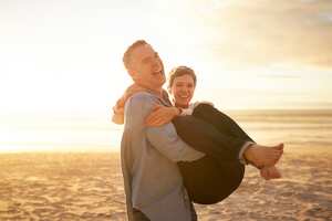 Mature man carrying girlfriend on the beach, at sunset