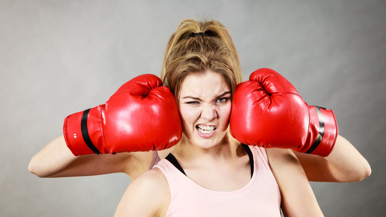 Sporty having head between boxing gloves, somebody punching her. Studio shot on grey background.