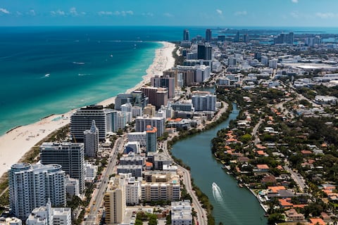 Aerial view of South Beach Miami Florida cityscape with buildings along the beach on a beautiful sunny day, people on beach and ocean, Collins Ave., and boat on Indian Creek