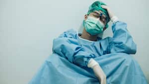 Médico con dolor de cabeza y cansado del trabajo mientras usa traje de PPE para proteger la enfermedad del coronavirus. El bienestar y la resiliencia emocional son componentes clave para mantener los servicios de atención esenciales.