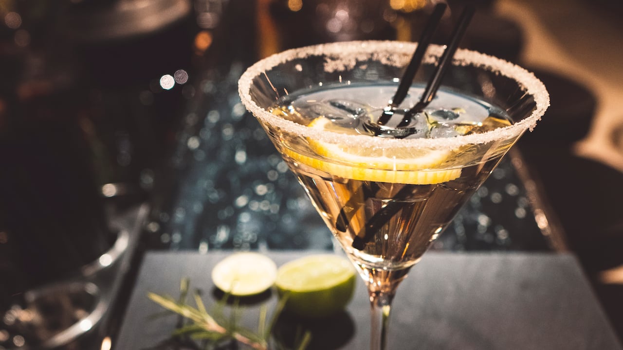 Glass of martini on a grnished surface with lemon slices and rosemary. Black bakground. Glas garnished with sugar on the edge.