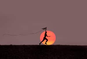 Boy playing with kite at sunset.