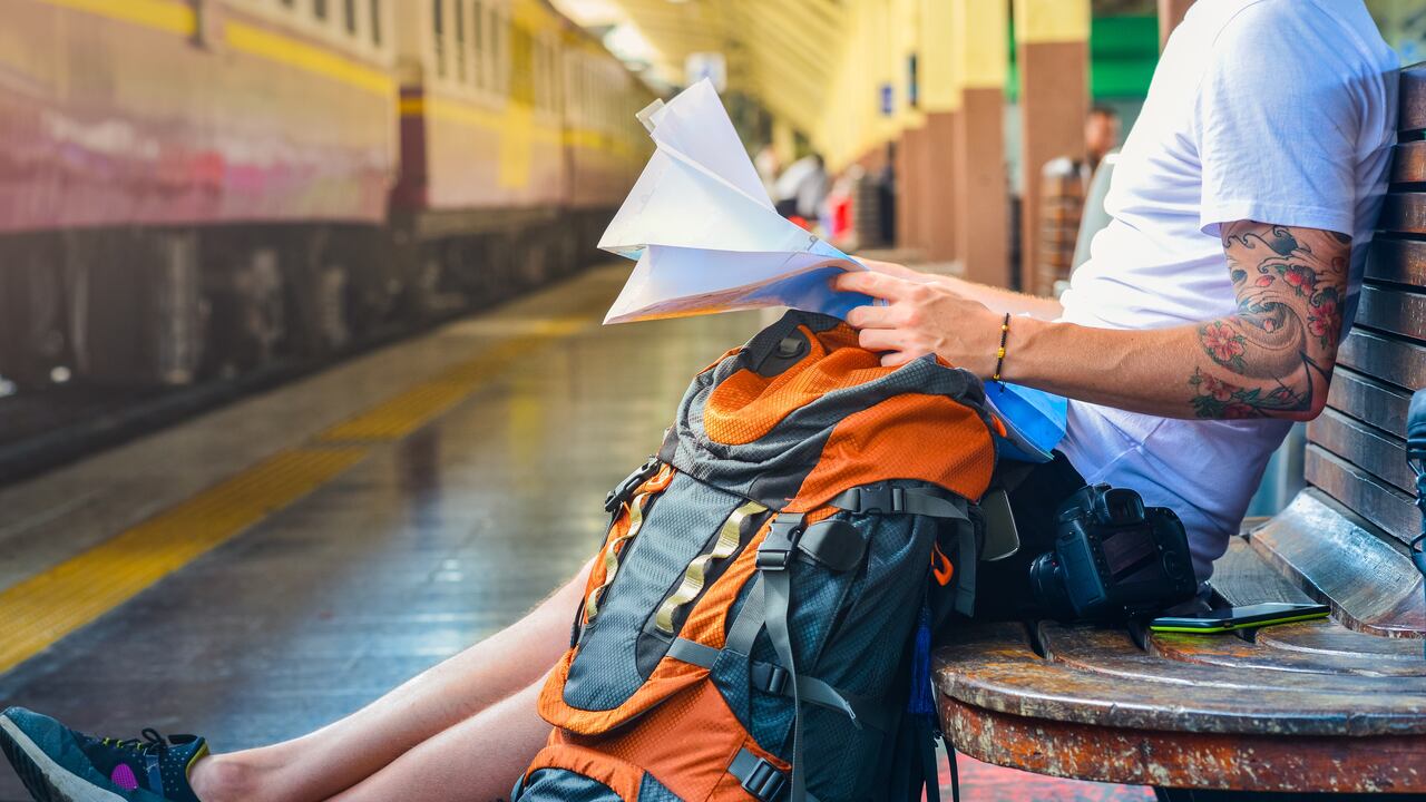 Hombre sentado revisando su plan de viaje con su maleta al lado