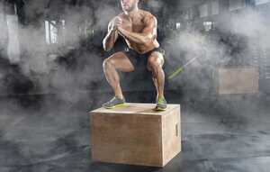 Bodybuilder man, does the cardio exercise, jumping on a wooden box in the gym. Sport concept, fat burning and a healthy lifestyle.
