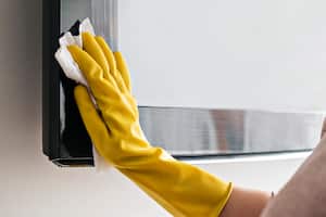 Woman cleaning the TV with damp cloths and wearing yellow gloves during coronavirus, covid 19 quarantine. Maintain hygiene at home, clean dust and bacteria, clean viruses from television.