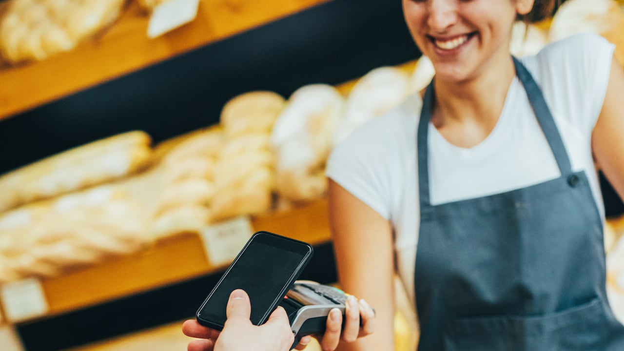 Joven haciendo un pago sin contacto a través de un teléfono inteligente en una panadería.