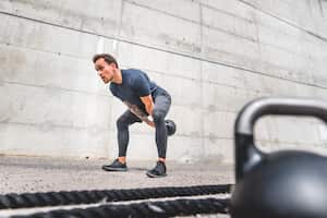 Low angle view of Caucasian athlete in mid 20s doing double-handed kettlebell swing with additional equipment in foreground.