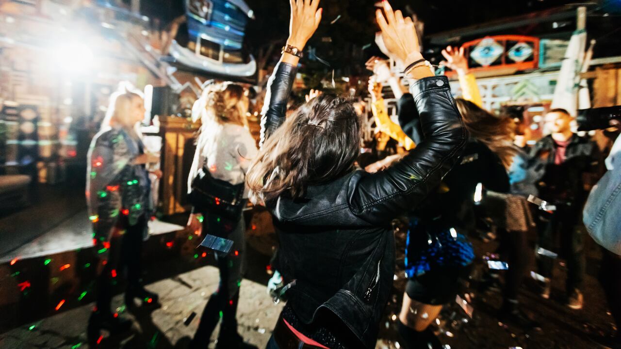 A young woman throwing her hands in the air, feeling the music and dancing energetically at a trendy open air nightclub