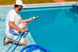 Mature man in flip flops cleaning the swimming pool with a vacuum cleaner. Man working as a cleaner of the swimming pool, he standing with special equipment for cleaning at poolside and working