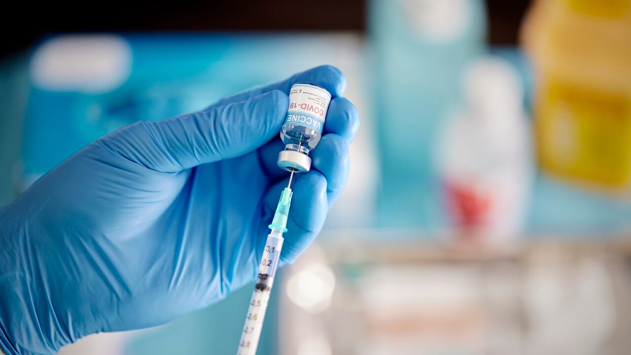 Un trabajador de la salud pone guantes quirúrgicos y saca el líquido de la vacuna COVID-19 del vial para vacunar a un paciente