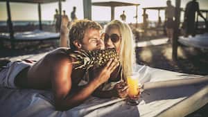 Joven pareja mordiendo una piña en una cama de playa