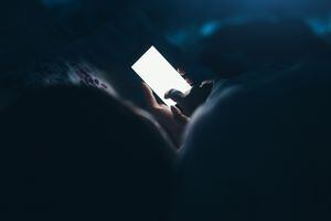 Woman texting and reading on smartphone in bed in midnight.