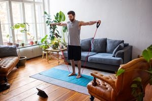 Hombre haciendo ejercicio con banda de estiramiento en casa con una tableta digital. Hombre adulto de mediana edad que usa una banda de goma elástica siguiendo un tutorial en línea y hace ejercicio en casa durante el aislamiento de Covid - 19 en casa.