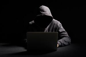 Persona irreconocible trabajando en una laptop en la oscuridad. Concepto de piratería de datos.